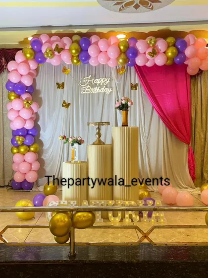 A simple but elegant butterfly theme with a pink and purple balloon arch on a stage.