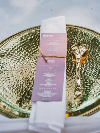 An elegant menu card tied with twine to a napkin, placed on a hammered gold thali. This shows how I coordinate even the smallest details with the overall event aesthetic.