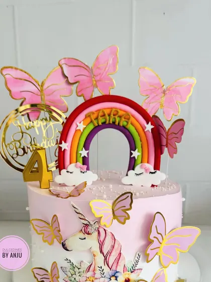 A magical unicorn and rainbow cake, adorned with pink butterflies and a golden "Happy Birthday" topper.