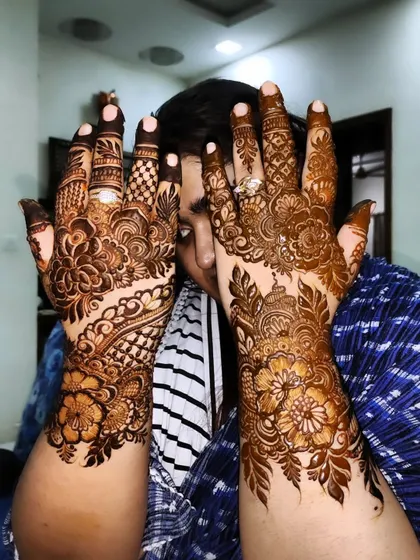 A happy client peeking through her beautifully adorned hands. The design is a mix of floral and geometric patterns.