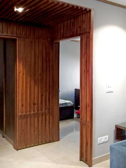 The wooden paneling system in the Gurgaon residence acts as both a wall surface and a doorway. The rhythmic pattern of the wood slats continues across the door, creating a seamless and integrated architectural element that defines the home's interior.