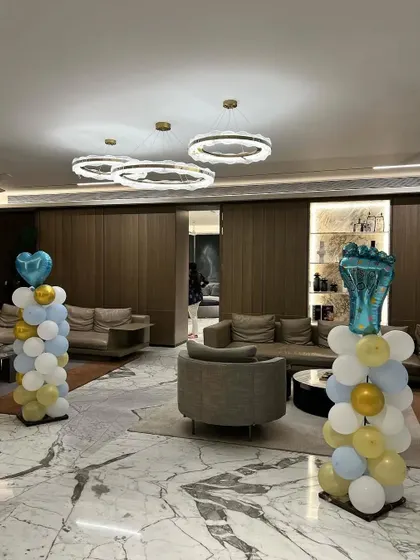 Simple yet elegant balloon pillars in pastel blue, white, and gold, used to decorate the entrance of a baby shower venue.
