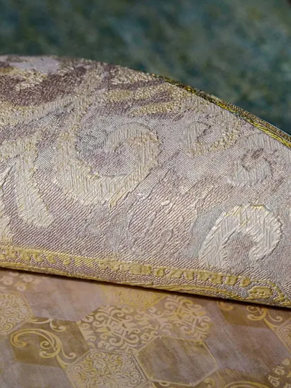 A close-up of a rolled-up classic wallpaper, showing the intricate pattern and texture. The combination of gold and beige in a traditional design creates a warm, luxurious feel.