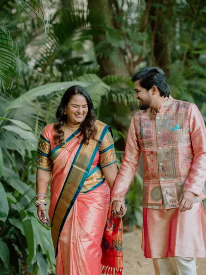 A candid shot of a couple walking and talking, holding hands in a garden. The natural interaction and their smiles show the comfortable and easygoing nature of their relationship.