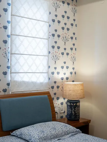 This bedroom showcases a beautiful blend of prints, with a floral wallpaper and matching roman blinds. The wooden bed and ceramic lamp add to the room's cozy, traditional charm.