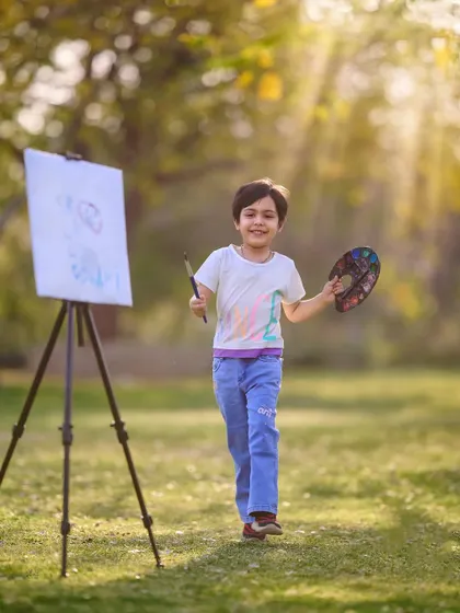 Proudly showing off his masterpiece. This action shot captures the happy energy of a young artist at work during his themed photoshoot in the park.
