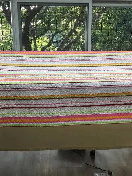 A bright, striped quilt displayed on a quilting frame.