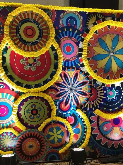 A creative and colorful backdrop for a Mehendi or Sangeet, using vibrant graphic prints accented with real marigold flowers. This fusion of modern art and traditional elements creates a fun and festive vibe.