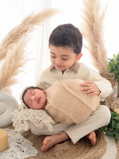 I love bringing creative themes to life, like this warm, boho-inspired setup. Here, a proud big brother holds his new sibling, showcasing how I can blend a stylized session with genuine family moments.