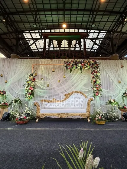 An elegant reception stage with a white and gold theme. The flowing drapes, floral arrangements, and hanging bells create a dreamy and romantic atmosphere.