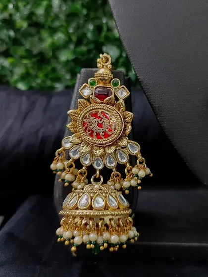 A stunning earring from a rental set, featuring a red carved stone and a classic jhumka drop. The design is inspired by traditional motifs.
