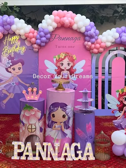A full view of the outdoor fairy theme birthday party. The setup includes a large marquee number '1', themed plinths, and character cutouts, all set on a red carpet.
