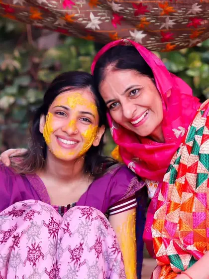 A classic portrait of a bride and her mother, both smiling brightly for the camera during the Haldi festivities. A beautiful memory of shared happiness.