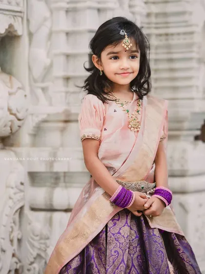 A young girl dressed beautifully in a traditional South Indian lehenga for Vara Mahalakshmi. The intricate details of her outfit and the temple-like background create a graceful and divine portrait.