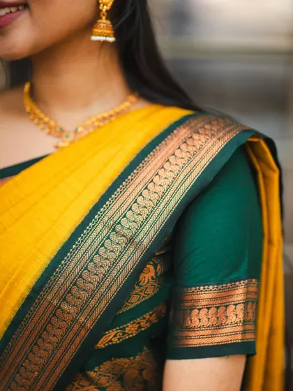 A detailed shot focusing on the shoulder and blouse of a yellow and green cotton saree. This highlights the intricate border weave and the texture of the fabric.