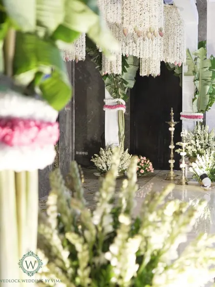 A detail shot of the decor for a traditional South Indian ceremony. The space is filled with fragrant jasmine garlands, banana leaf pillars, and brass lamps, creating an authentic and sacred ambiance.