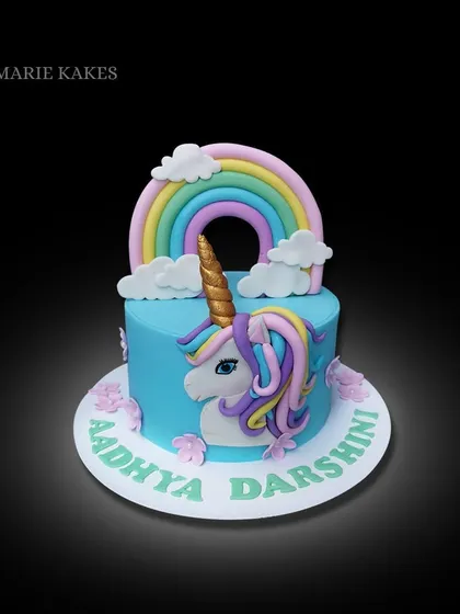 A magical unicorn cake with a rainbow topper. This design features a 2D unicorn face on the side of the cake, surrounded by pastel flowers and the birthday girl's name.