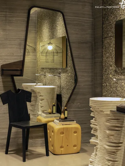 This powder bathroom embraces an artistic approach to spatial design. With its quirky blend of elements, including a sculptural stacked-stone basin, an asymmetric mirror, and dramatic lighting, every detail comes together to infuse the space with a sense of spectacle.
