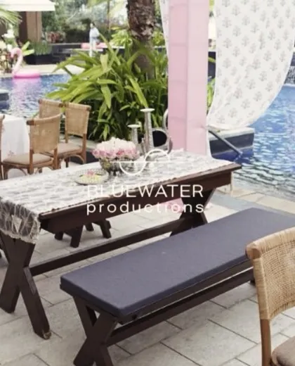A simple yet chic poolside dining setup for a Haldi, with dark wood benches and tables accented by delicate floral centerpieces.