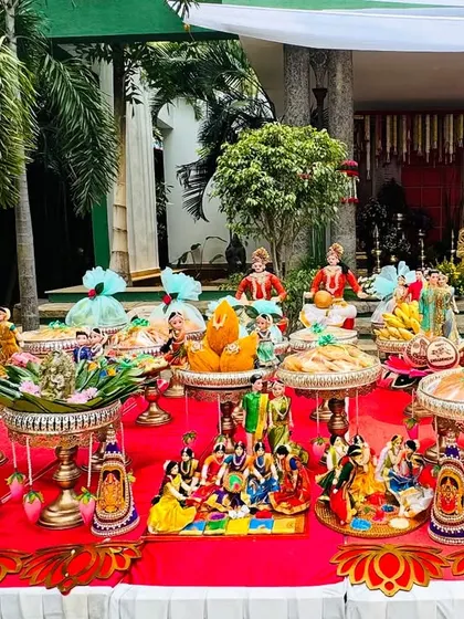 An outdoor platter setup with a bright red theme. The dolls, fruits, and sweets are arranged on a long table, creating a festive and welcoming display for guests.