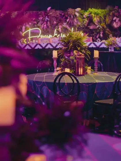 A view of the candlelit tables and neon signs being arranged for a glamorous cocktail night.