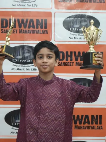 A young student holds up two trophies, showcasing his versatile talent.