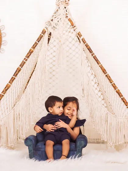A sweet moment between siblings in a boho-themed teepee setup in the studio. The older sister protectively holds her younger brother.