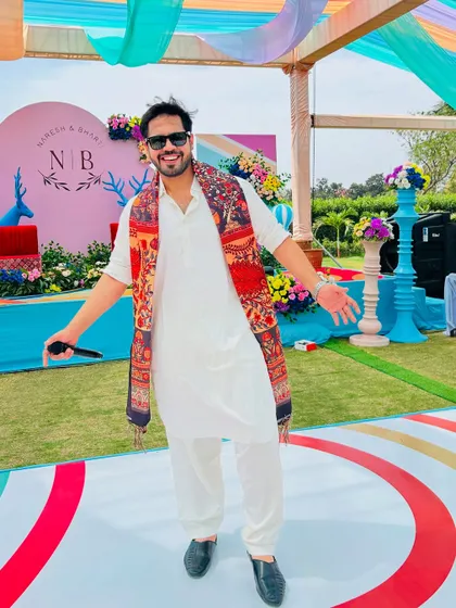 A full shot of me on the colorful stage of a Mehendi carnival, dressed in a white kurta that stands out against the vibrant decor.