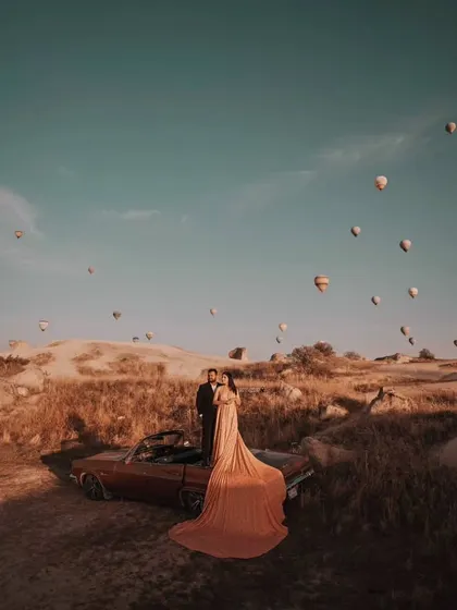 The long trail of the peach gown drapes beautifully over the vintage car, creating a romantic and cinematic feel for this destination pre-wedding shoot.