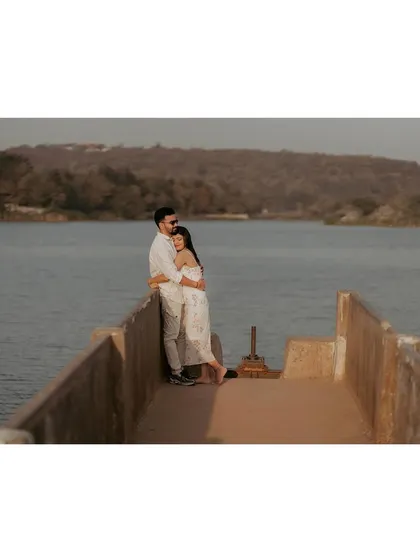 A couple embraces at the end of a pier, looking out over the water together in a peaceful, shared moment.