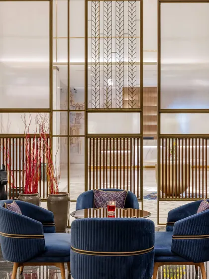 Intricately designed metal and glass screens separate the lounge from the lobby, offering privacy without enclosure. These bespoke elements feature patterns that add a layer of sophistication and visual interest to the space.