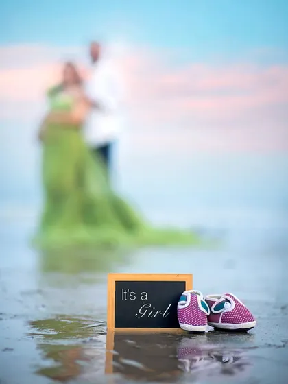 "It's a Girl!" A creative announcement shot focusing on the tiny shoes and sign, with the happy parents blurred softly in the background.
