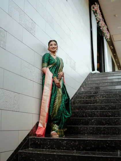 A full view of this stunning bride on the stairs. Her green and gold paithani saree is draped to perfection, and her elegant updo completes the regal look.