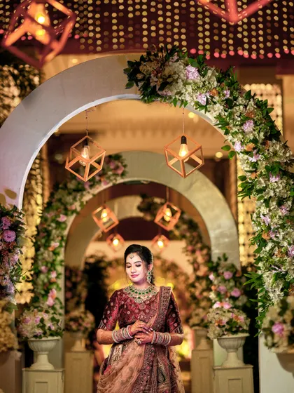 A solo portrait of the bride standing under a floral arch with geometric lanterns, looking radiant.