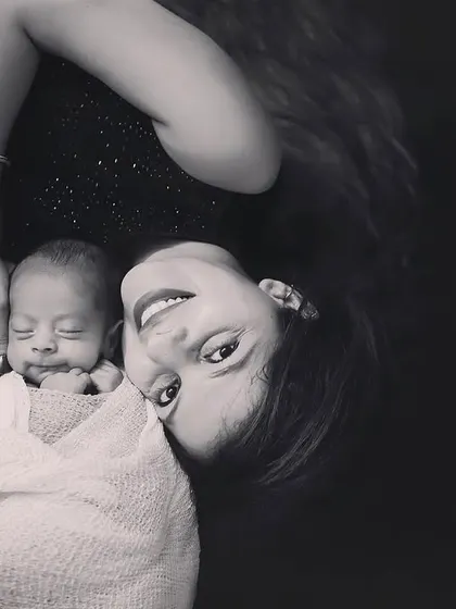 A beautiful black and white portrait of a mother and her newborn. The creative angle and her bright smile looking up at the camera make this a truly unique and artistic shot.