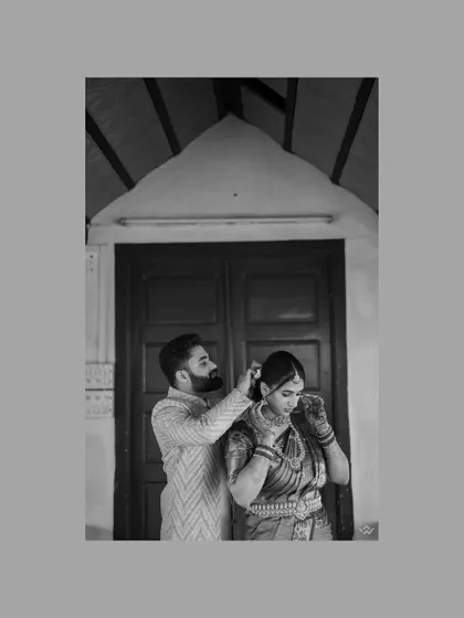 A creative black and white portrait of the groom helping the bride with her jewelry, a small, intimate gesture of care.