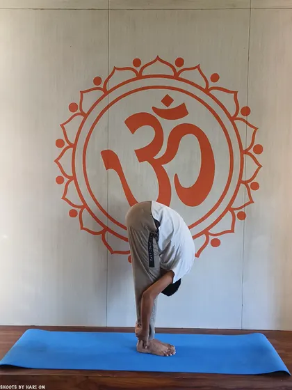 A student practices Padahastasana (Hand to Foot Pose), a forward bend that calms the mind and stretches the entire back side of the body.