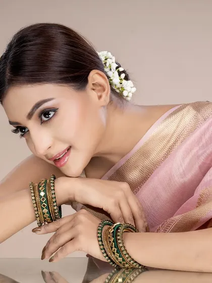 A reflective shot of the model leaning on a surface, offering a different perspective on the green bangles and pink saree combination.
