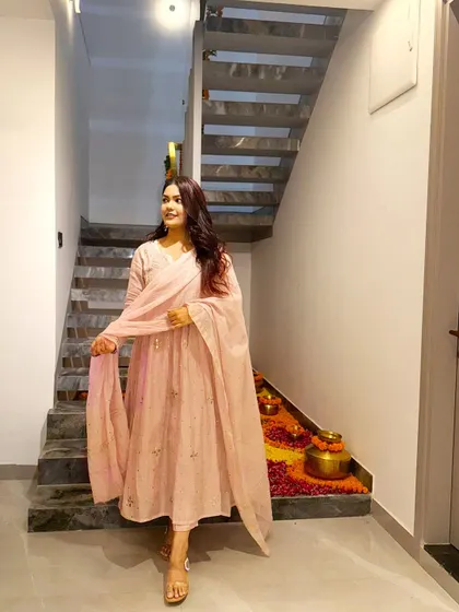 Another view of the pastel pink Anarkali, showing the festive decorations in the background that complement the outfit's vibe.