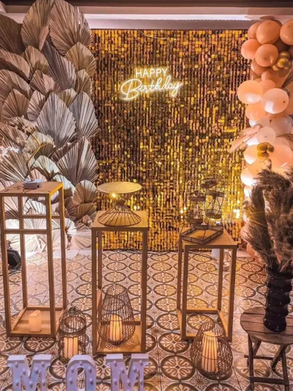 A chic setup for "Mom's" birthday, featuring a gold sequin wall, dried palm leaves, and a neon sign.