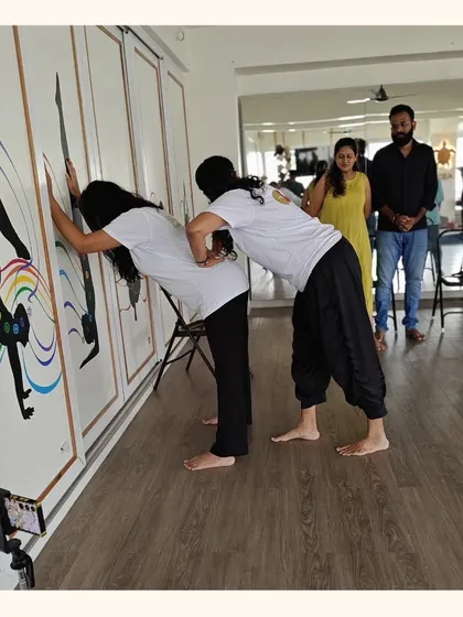 A teacher provides support as an expectant mother practices a wall-assisted stretch. Our prenatal classes focus on safe, modified movements that accommodate the changing body.