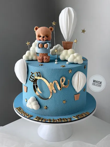 A dreamy first birthday cake with a teddy bear and hot air balloon theme. This elegant blue cake features a textured velvet finish and handcrafted details.