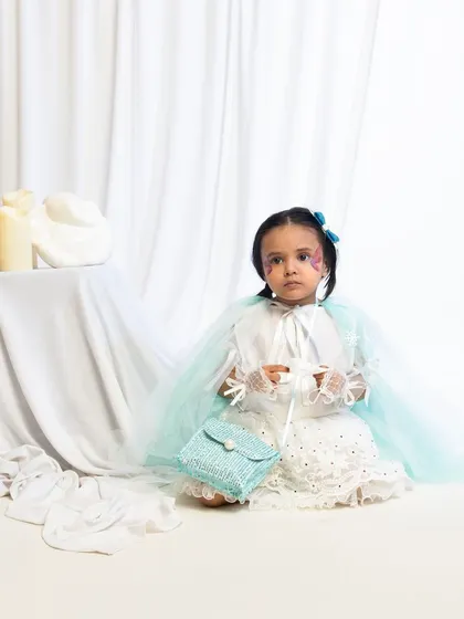 A child model seated in a white and green fairy costume, holding a small purse.