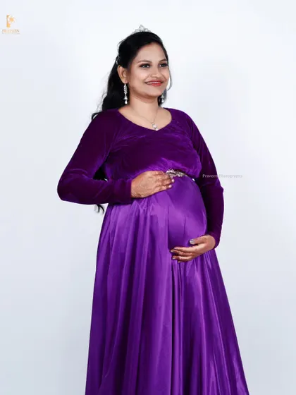 This side-profile shot beautifully highlights the baby bump in the purple maternity gown. The velvet top and satin skirt create a lovely textural contrast.
