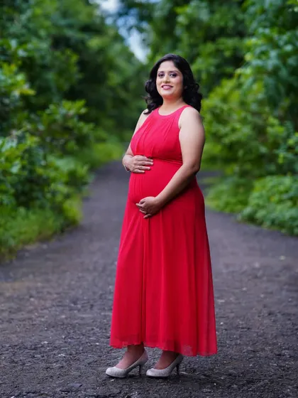 A solo portrait of the mother-to-be in a vibrant red dress, standing on a path in a green park. The natural setting complements her radiant glow.