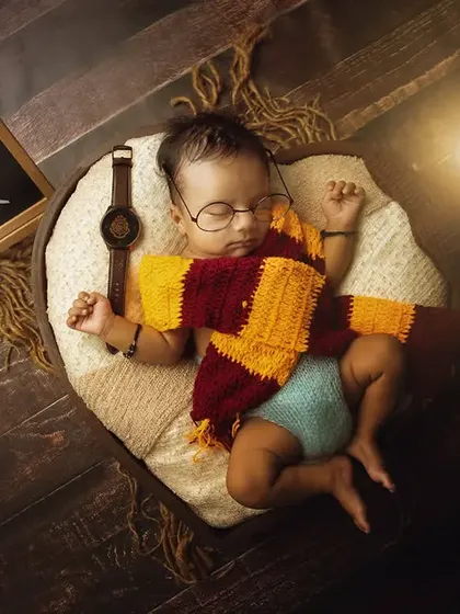 A full Harry Potter themed newborn setup, with the baby wearing glasses and a scarf, complete with a wand and a chalkboard sign.
