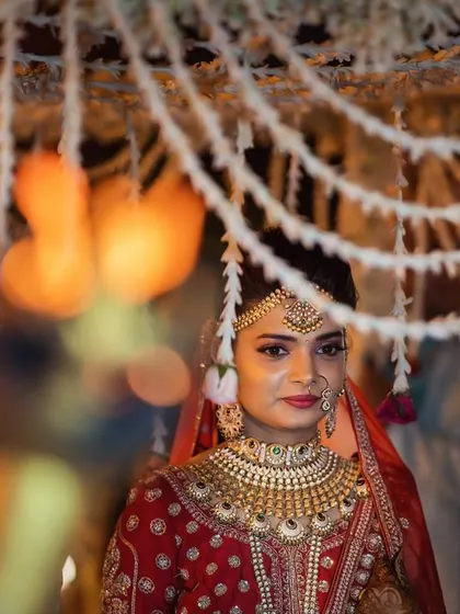 A bride framed by hanging floral decorations. The soft focus and warm lights create a dreamy, romantic atmosphere, highlighting her calm and beautiful presence.