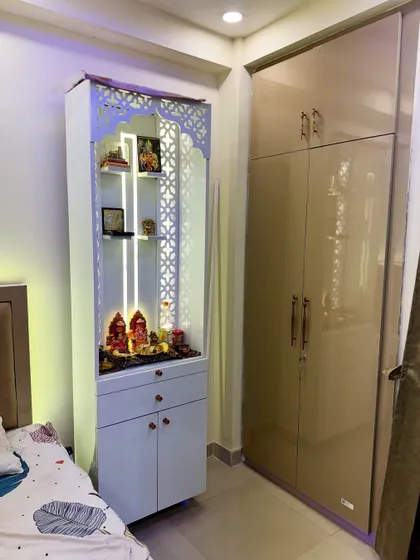 A close-up of a beautiful mandir unit designed to fit in a bedroom corner. It features CNC-cut jali work, internal lighting, and drawers for storage.