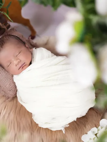 A beautifully framed shot of a sleeping newborn, viewed through a soft floral foreground. This technique creates an intimate and gentle portrait, focusing on the baby's peacefulness.