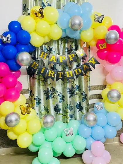 A colorful rainbow-themed birthday balloon ring with butterfly accents.